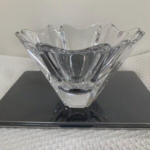 May include: A clear, faceted glass bowl with a unique, scalloped rim design. The bowl has a square base and a smaller, rounded bowl nested inside. The glass is transparent, allowing light to pass through, and is likely used for decorative purposes.