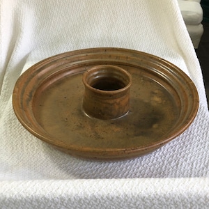 May include: A brown ceramic serving dish with a central well. The dish has a speckled glaze and a slightly raised rim.
