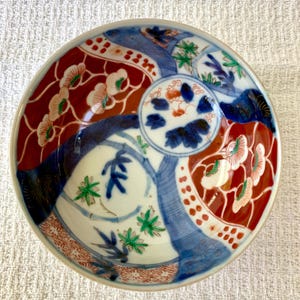 May include: A decorative ceramic bowl with a detailed, colorful design. The bowl features a white interior with blue, red, and green floral and geometric patterns. The rim is a light beige color. The bowl is likely used for serving or display.