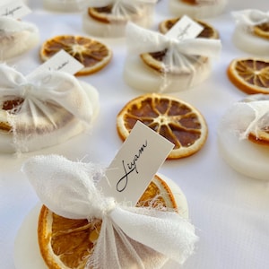 Pode incluir: Cart&otilde;es de lugar circulares brancos com fatias de laranja secas amarradas com tecido branco e uma etiqueta de nome escrita &agrave; m&atilde;o. A etiqueta de nome diz "Liam".