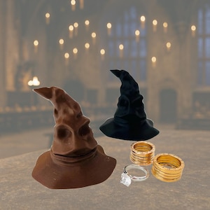 Peut inclure: Deux chapeaux de sorcier, un marron et un noir, sont présentés à côté de trois bagues dorées et une bague argentée avec une grosse pierre transparente. Les chapeaux rappellent le Choixpeau magique.