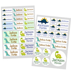 May include: A set of 24 personalised name labels featuring a dinosaur theme. The labels depict a green and blue dinosaur with the name "Jackson Fortin" printed on them. The labels come in a variety of shapes and sizes, including rectangular, oval, and circular.