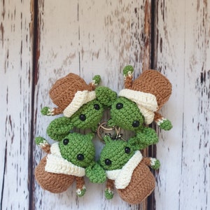 May include: Four crocheted green and brown baby Yoda keychains with white trim. The keychains are arranged in a circle on a white wooden background.