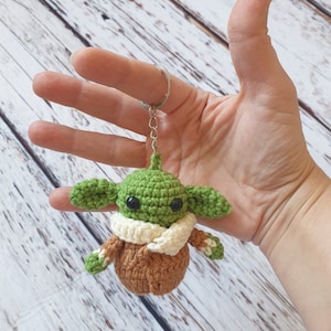 May include: Green crocheted keychain with a brown coat and a white scarf. The keychain is shaped like a popular fictional character.
