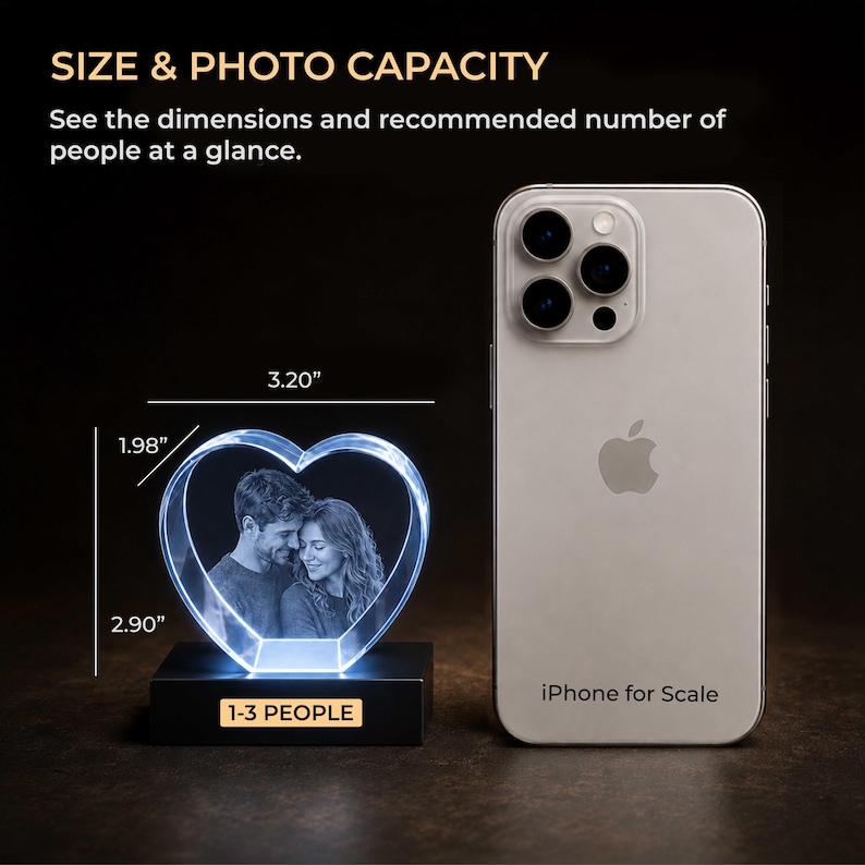 May include: A heart-shaped crystal block featuring an engraved image of a couple, mounted on a black base labeled 1-3 PEOPLE. Dimensions are 3.20 inches wide by 1.98 inches high, with a total height of 2.90 inches, shown next to an iPhone for scale.
