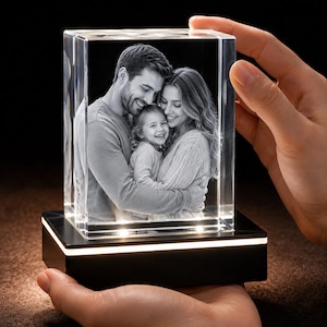 May include: A rectangular glass block featuring a laser-etched black and white photograph of a family of three embracing. The clear glass block sits atop a black rectangular base with an integrated light strip that illuminates the crystal from below.
