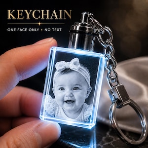 May include: A rectangular crystal keychain featuring a laser-engraved black and white portrait of a baby wearing a bow headband. The crystal is illuminated with a blue light and attached to a silver-toned metal chain and ring. Text reads KEYCHAIN.
