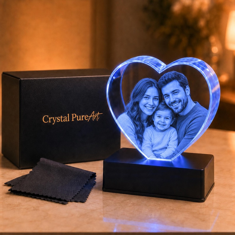 May include: A heart-shaped crystal block featuring a laser-etched photograph of a woman, a man, and a child. The crystal is illuminated by a blue LED light and sits on a black rectangular base. A black gift box with the text Crystal PureArt is included.