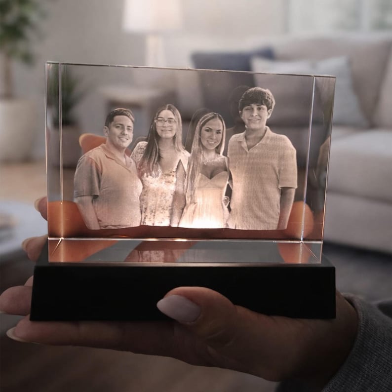 May include: A rectangular clear glass block featuring a laser-etched three-dimensional portrait of four people standing side by side. The glass block is mounted on a solid black rectangular base that illuminates the image from below.
