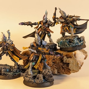 Könnte beinhalten: Miniaturfiguren futuristischer Soldaten in silberner, goldener und schwarzer Rüstung, bewaffnet mit Gewehren und Pistolen. Die Figuren posieren auf felsigem Gelände, einige stehen auf Sockeln, die an Wasser erinnern. Das Gesamtthema ist Science-Fiction.