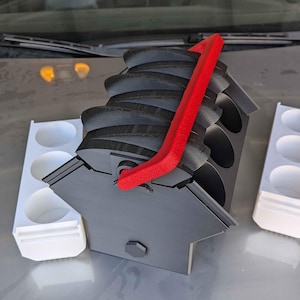 May include: A black 3D printed paint pot holder with a red handle. The holder has six slots for paint pots and is designed to be compact and portable.