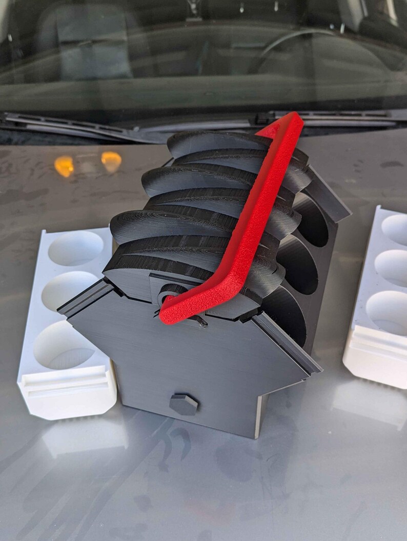 May include: A black 3D printed paint pot holder with a red handle. The holder has six slots for paint pots and is designed to be compact and portable.