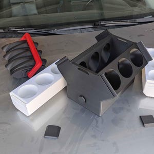 May include: Three white plastic cup holders with black and red plastic cup holders. The cup holders are on a silver surface.