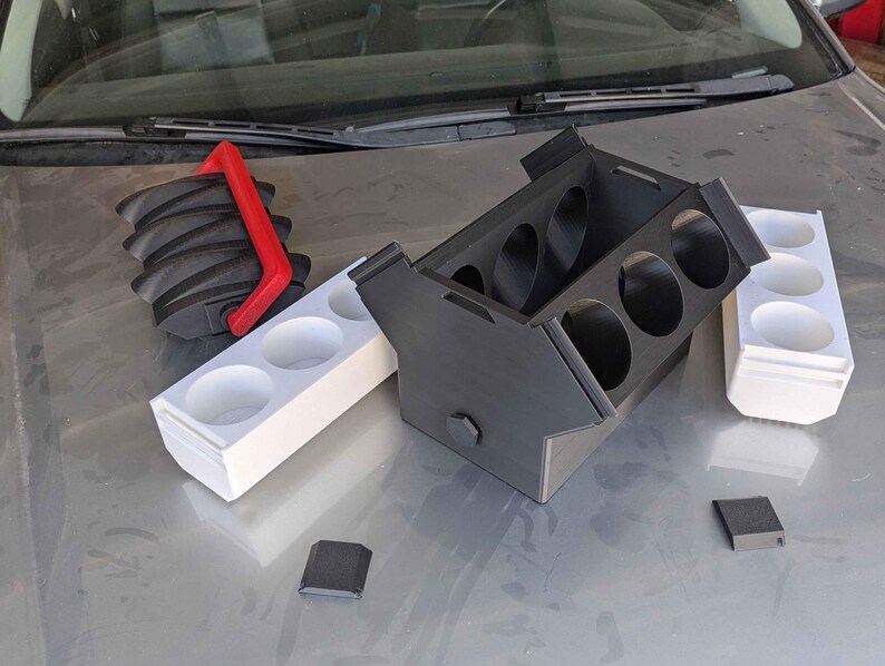 May include: Three white plastic cup holders with black and red plastic cup holders. The cup holders are on a silver surface.