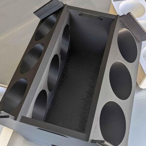 May include: A black wooden box with a hinged lid and six round compartments. The box is open and the compartments are empty.