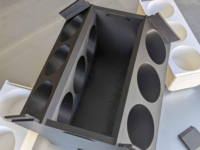 May include: A black wooden box with a hinged lid and six round compartments. The box is open and the compartments are empty.