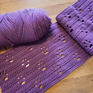 May include: A purple crocheted scarf with a lacy pattern. A ball of purple yarn is also in the image.