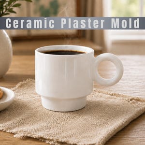 May include: A white ceramic mug with a cylindrical body, a stepped base, and a circular handle, filled with dark coffee. The text Ceramic Plaster Mold is displayed in a grey banner across the top of the image, which also shows steam rising.