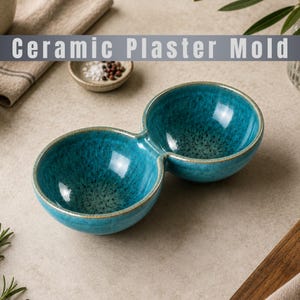 Pode incluir: Um molde de gesso cerâmico de tigela dupla com um esmalte azul turquesa vibrante, acabamento salpicado e interior liso e arredondado. O texto Ceramic Plaster Mold é exibido numa faixa cinzenta no topo da imagem.