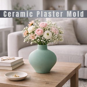 May include: A light green ceramic vase holding a bouquet of pink, white, and peach flowers. The vase sits on a wooden table with a small white dish and a stack of books. The text "Ceramic Plaster Mold" is above the vase.