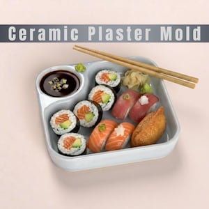 May include: A light gray square ceramic plaster mold with a rounded corner compartment for soy sauce. The dish contains assorted sushi rolls, nigiri, and ginger, with a pair of wooden chopsticks resting across the top. Text reads Ceramic Plaster Mold.