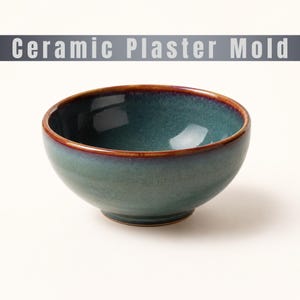 Puede incluir: Un cuenco de cerámica redondo con un esmalte interior y exterior en azul verdoso profundo, con un borde marrón distintivo. El texto Ceramic Plaster Mold aparece en una franja gris en la parte superior de la imagen sobre un fondo blanco.