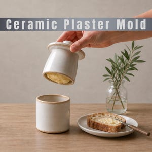 May include: A white ceramic butter dish with a lid, held open to reveal butter. The base is cylindrical, and a slice of bread with butter sits on a small plate. The text "Ceramic Plaster Mold" is at the top.