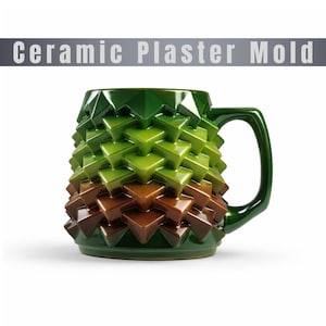 May include: A ceramic mug with a geometric design, featuring a gradient of colors from brown to green. The mug has a handle and the text "Ceramic Plaster Mold" is above the mug.
