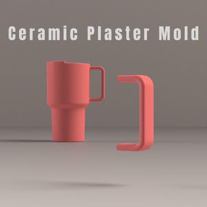 May include: A coral-coloured ceramic plaster mould for a mug with a handle, featuring the text "Ceramic Plaster Mold" at the top. The mould consists of a cylindrical body with an attached handle and a separate, detached U-shaped handle piece.