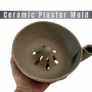 Puede incluir: Un molde de yeso cerámico de color marrón claro para exprimidor de cítricos, con un cono central rodeado por cuatro ranuras de drenaje y un pico vertedor lateral. El texto "Ceramic Plaster Mold" aparece en letras blancas en la parte superior.