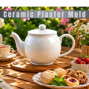 Puede incluir: Una tetera de cerámica blanca con tapa a juego, que presenta un cuerpo redondeado, un pico curvo y un asa. El texto "Ceramic Plaster Mold" aparece en la parte superior de la imagen. La tetera se encuentra sobre una superficie de madera con galletas.