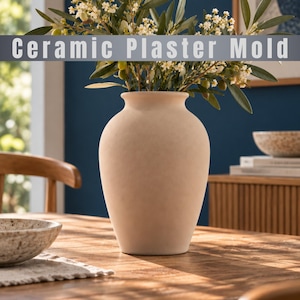 Può includere: Un vaso in stampo di gesso ceramico color beige opaco con corpo arrotondato e bordo svasato. Il vaso è riempito con rami di ulivo verdi con piccoli fiori bianchi. Il testo "Ceramic Plaster Mold" è visualizzato su una fascia grigia in alto.