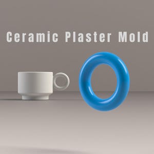 May include: A white ceramic cup with a circular handle and a bright blue ring-shaped object. The text "Ceramic Plaster Mold" is displayed in white letters above the objects. The background is a neutral gray.