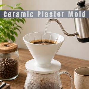 Op de afbeelding: Een witte keramische koffiefilter met verticale ribbels aan de binnenkant staat op een glazen karaf. Een roestvrijstalen zwanenhalsketel giet water in de filter. De tekst Ceramic Plaster Mold staat bovenaan de afbeelding.