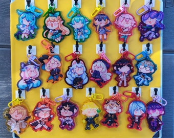 May include: A collection of colorful acrylic charm keychains featuring anime-style character designs. Each keychain has a unique character with vibrant colors and attached to a metal clasp. The keychains are displayed on a yellow pegboard.