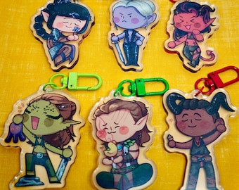 May include: A collection of acrylic keychains featuring fantasy character illustrations. Each keychain has a unique design with vibrant colors, including characters with horns, swords, and various accessories. The keychains have colored clasps.