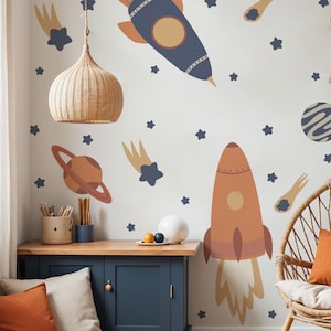May include: A white wall with a space-themed mural featuring two rockets, a planet, shooting stars, and stars. The rockets are orange and blue with yellow accents. The planet is orange with a ring around it. The stars are blue and yellow. The mural is perfect for a child's bedroom.