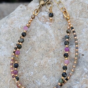 May include: A double-strand bracelet with a gold clasp and a variety of pink, green, and black beads.