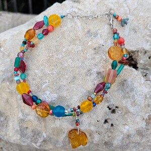 May include: A multi-strand anklet with a variety of colorful glass beads, including red, orange, yellow, green, and blue. The anklet has a silver clasp and a dangling charm in the shape of a leaf.