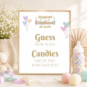 May include: A framed sign with the text "Happiest Baby Shower On Earth" and "Guess How Many Candies Are In The Baby Bottle?". The sign has a gold frame and is decorated with pastel-colored balloons and a baby bottle filled with candies.