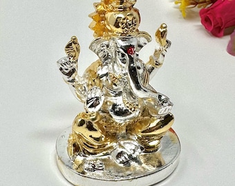 May include: A metallic figurine of the deity Ganesha, featuring a dual-tone gold and silver finish. The figure is depicted in a seated position on a circular base, adorned with a crown, a small red dot on the forehead, and four arms holding objects.
