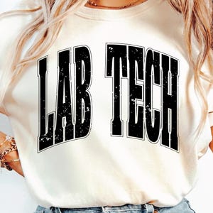 May include: Cream-colored sweatshirt with the text "LAB TECH" in bold, distressed black lettering. The text is centered and takes up a large portion of the shirt's front. The sweatshirt has a crew neck.