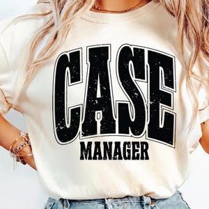 May include: Cream-colored sweatshirt with the words "CASE MANAGER" in a bold, distressed black font. The text is centered on the front of the shirt, creating a simple yet impactful design. The sweatshirt has a classic crew neck.