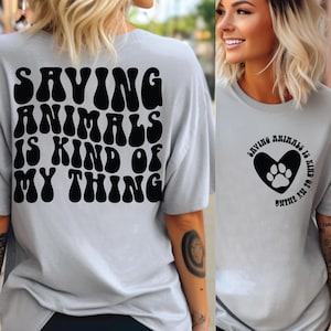 May include: A gray t-shirt with a black graphic that says "Saving Animals is Kind of My Thing" in a retro font. The back of the shirt has a black heart with a paw print inside and the same text in a circle.