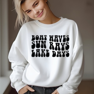 Op de afbeelding: Witte sweatshirt met de tekst "BOAT WAVES SUN RAYS LAKE DAYS" in een zwarte retro lettertype. De sweatshirt is effen wit en heeft een ronde hals.