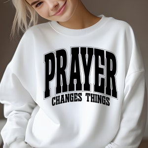 Peut inclure: Sweat-shirt blanc avec un texte noir qui dit "PRAYER CHANGES THINGS" dans une police de caractères audacieuse de style universitaire.