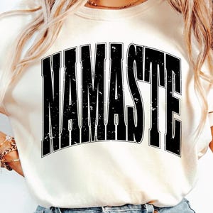 Op de afbeelding: Crèmekleurige sweatshirt met het woord "NAMASTE" gedrukt in grote, versleten zwarte letters. De tekst is gecentreerd en heeft een vintage, versleten uitstraling. De sweatshirt is een casual, comfortabele stijl.