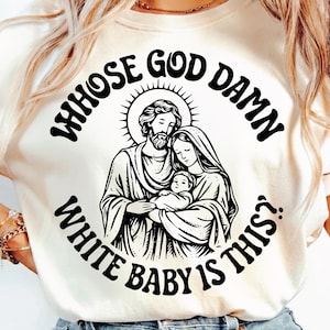 May include: Cream-colored t-shirt featuring a graphic of a religious family with the text "WHOSE GOD DAMN WHITE BABY IS THIS?" in a circular design. The graphic is in black and white.