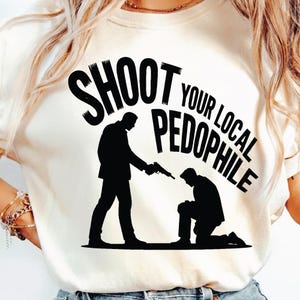 Puede incluir: Camiseta color crema con un gráfico negro que representa a una persona apuntando con un arma a otra persona arrodillada. El texto "SHOOT YOUR LOCAL PEDOPHILE" está impreso en negro sobre las figuras.