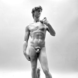 May include: A monochromatic gray sculpture of a standing figure with curly hair, depicted in a contrapposto stance with one hand raised toward the shoulder and the other resting at the side, set upon a textured, irregular stone-like base.